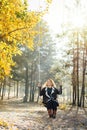 Young caucasian blonde woman in brown cardigan riding a swing in yellow autumn forest. Vertical orientation