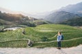 Young Caucasian blonde woman in denim shirt overlooking Sapa rice terraces at sunset in Lao Cai province, Vietnam