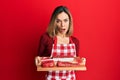 Young caucasian blonde woman holding board with raw meat in shock face, looking skeptical and sarcastic, surprised with open mouth Royalty Free Stock Photo