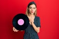 Young caucasian blonde woman holding vinyl disc relaxed with serious expression on face