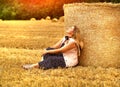 Young caucasian blonde woman sitting on a mown wheat field near a huge sheaf of hay enjoying nature at sunset. People and travel. Royalty Free Stock Photo