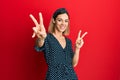 Young caucasian blonde woman wearing beautiful black and white dress smiling looking to the camera showing fingers doing victory Royalty Free Stock Photo