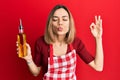 Young caucasian blonde woman wearing cook apron holding olive oil bottle looking at the camera blowing a kiss being lovely and