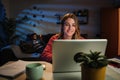 Young caucasian blonde woman working on her startup with laptop at home office sitting on desk at night. Happy female Royalty Free Stock Photo