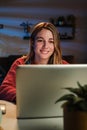 Vertical portrait of young woman working on her startup with laptop at home office sitting on desk at night. Happy Royalty Free Stock Photo