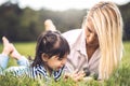 Young Caucasian blonde woman lying on the green grass and playing with0 her little kid girl in the park. Loving mother and Royalty Free Stock Photo