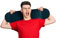 Young caucasian boy with ears dilation holding skate over shoulders angry and mad screaming frustrated and furious, shouting with Royalty Free Stock Photo