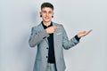 Young caucasian boy with ears dilation wearing business jacket amazed and smiling to the camera while presenting with hand and Royalty Free Stock Photo