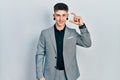 Young caucasian boy with ears dilation wearing business jacket smiling and confident gesturing with hand doing small size sign Royalty Free Stock Photo