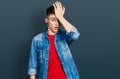 Young caucasian boy with ears dilation wearing casual denim jacket surprised with hand on head for mistake, remember error