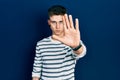 Young caucasian boy with ears dilation wearing casual striped shirt doing stop sing with palm of the hand