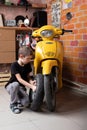 A young Caucasian boy is very focused, picks up a tire on his yellow motorcycle scooter on his own. Stylish workshop