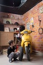A young Caucasian boy is very focused, picks up a tire on his yellow motorcycle scooter on his own. Stylish workshop