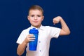 Young caucasian boy wearing white t-shirt holding water bottle happy shows how he is strong on blue wall