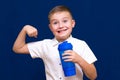 Young caucasian boy wearing white t-shirt holding water bottle happy shows how he is strong on blue wall