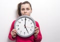 Young caucasian brunette girl with grin on her face holds round clock against white wall background Royalty Free Stock Photo