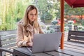 Young Caucasian business woman with blonde hair working on laptop in outdoor cafe. College student using technology Royalty Free Stock Photo