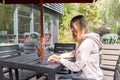 Young Caucasian business woman with blonde hair working on laptop in outdoor cafe. College student using technology Royalty Free Stock Photo