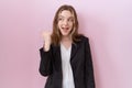 Young caucasian business woman wearing black jacket smiling with happy face looking and pointing to the side with thumb up Royalty Free Stock Photo