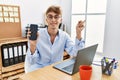 Young caucasian businessman working using laptop and showing smartphone smiling happy pointing with hand and finger to the side Royalty Free Stock Photo