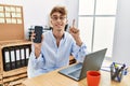 Young caucasian businessman working using laptop and showing smartphone smiling with an idea or question pointing finger with Royalty Free Stock Photo