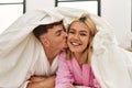 Young caucasian couple covering with bedsheet and smiling happy lying on the bed at home Royalty Free Stock Photo