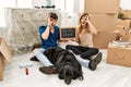 Young caucasian couple with dog holding our first home blackboard at new house doing ok gesture shocked with surprised face, eye