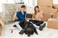 Young caucasian couple with dog holding our first home blackboard at new house smiling positive doing ok sign with hand and