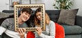 Young caucasian couple with dog making family picture holding empty frame at home