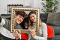 Young caucasian couple with dog making family picture holding empty frame at home