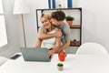 Young caucasian couple hugging and kissing using laptop sitting on the desk at home Royalty Free Stock Photo