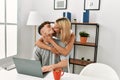 Young caucasian couple hugging and kissing using laptop sitting on the desk at home Royalty Free Stock Photo