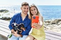 Young caucasian couple make selfie by the smartphone sitting on the bench with dog at the beach Royalty Free Stock Photo