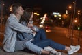 Young caucasian couple is sitting on the pavement hugging each other against the backdrop of the lights of the night city. Date Royalty Free Stock Photo