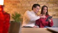 Young caucasian couple sitting on sofa smilingly watching into tablet in home atmosphere.