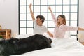 Young caucasian couple smiling happy stretching arms waking up lying on the bed with dog at home