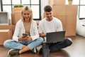 Young caucasian couple smiling happy using laptop and smartphone sitting at new home Royalty Free Stock Photo