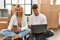 Young caucasian couple smiling happy using laptop and smartphone sitting at new home Royalty Free Stock Photo