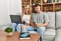 Young caucasian couple smiling happy using laptop and smartphone sitting on the sofa at home Royalty Free Stock Photo