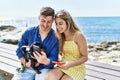 Young caucasian couple using smartphone sitting on the bench with dog at the beach Royalty Free Stock Photo