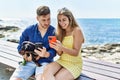 Young caucasian couple using smartphone sitting on the bench with dog at the beach Royalty Free Stock Photo