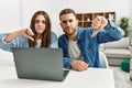 Young caucasian couple working using computer laptop at home with angry face, negative sign showing dislike with thumbs down, Royalty Free Stock Photo
