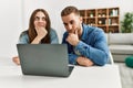 Young caucasian couple working using computer laptop at home serious face thinking about question with hand on chin, thoughtful Royalty Free Stock Photo
