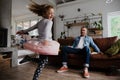 Young daughter dancing around while father happy spectates on sofa of living room