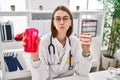 Young caucasian dentist woman holding denture and mouthwash puffing cheeks with funny face