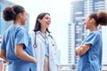 Young caucasian doctor in a lab coat standing outside and talking to mixed race nurses in scrubs. Diverse group of Royalty Free Stock Photo