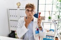 Young caucasian doctor man holding ear otoscope at the clinic covering mouth with hand, shocked and afraid for mistake Royalty Free Stock Photo