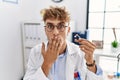 Young caucasian doctor man holding earing aid at the clinic covering mouth with hand, shocked and afraid for mistake Royalty Free Stock Photo