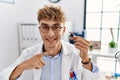 Young caucasian doctor man holding earing aid at the clinic smiling happy pointing with hand and finger