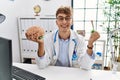 Young caucasian doctor man wearing doctor coat holding brain at the clinic screaming proud, celebrating victory and success very Royalty Free Stock Photo